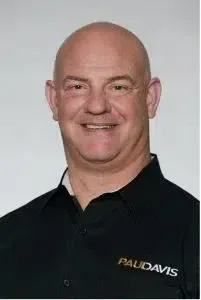Smiling bald man in a black polo shirt with a PAU Davis logo on the chest.