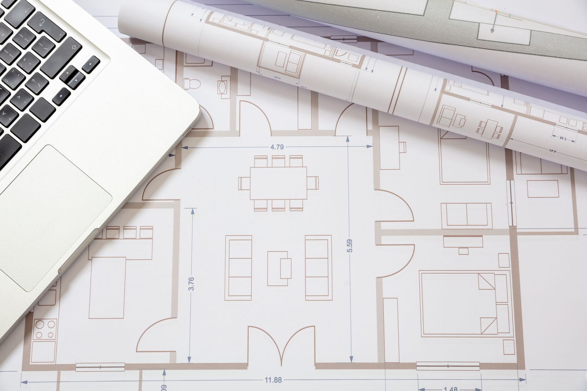 Laptop on architectural floor plans with a rolled blueprint on a white desk