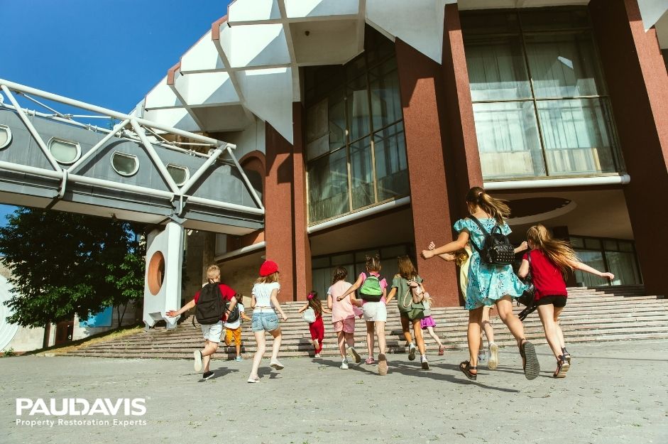 Group of children running towards a large building on a sunny day.