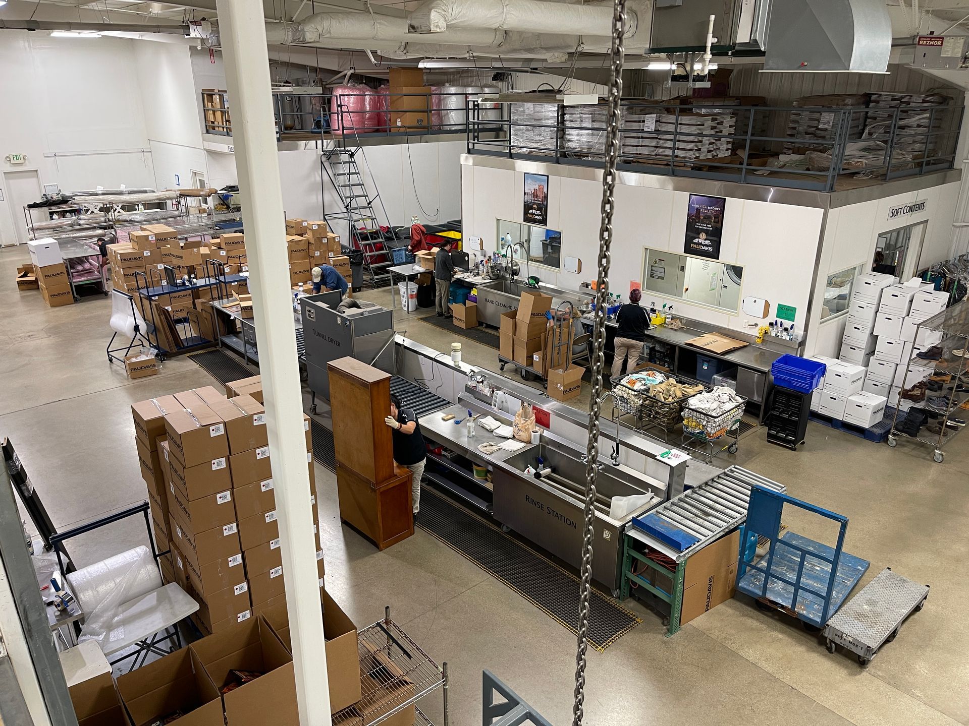 An overhead view of a busy warehouse with boxes, equipment, workstations, and people working on a concrete floor.