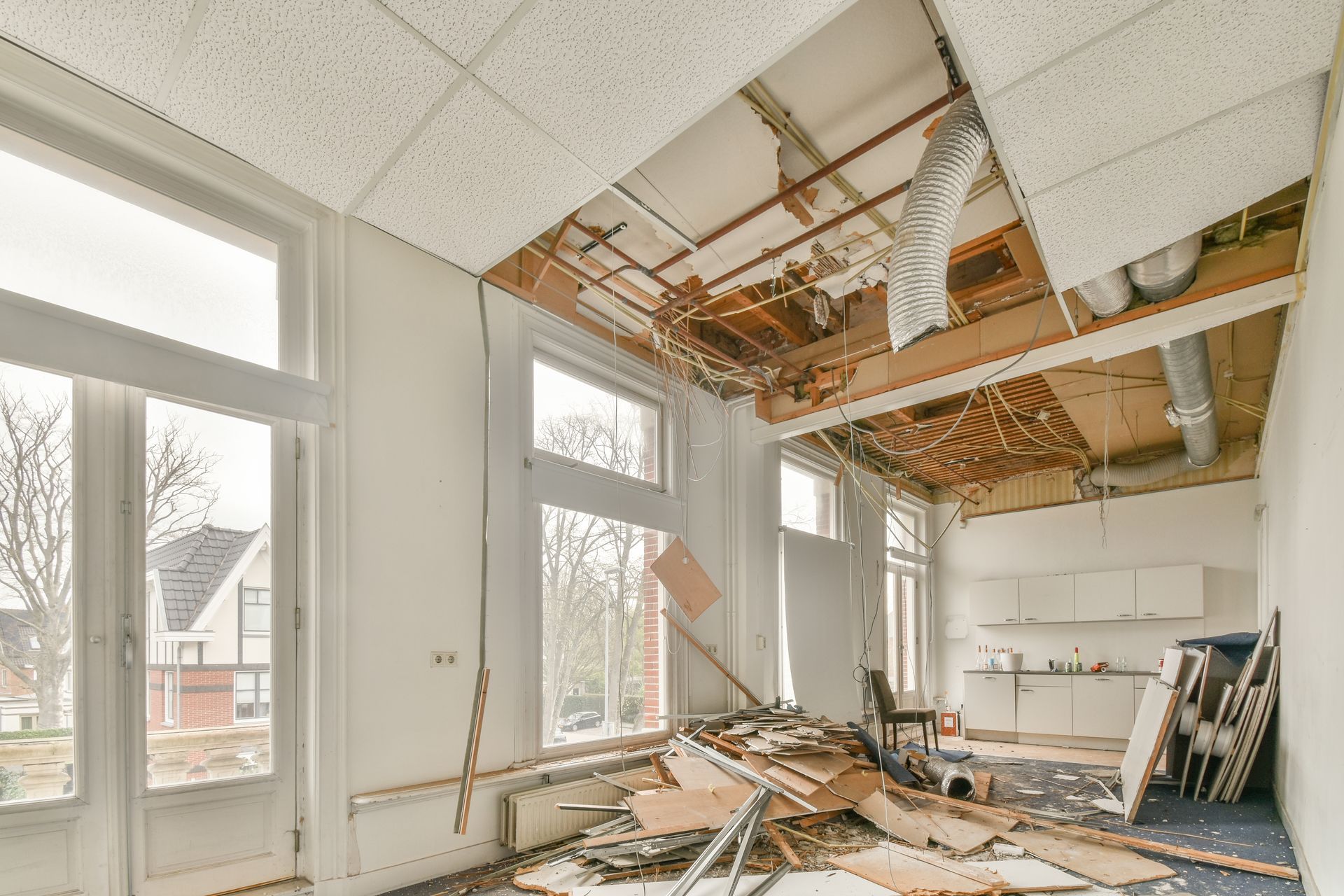 Severely damaged office with collapsed ceiling panels, exposed ducts, and debris scattered on the floor.