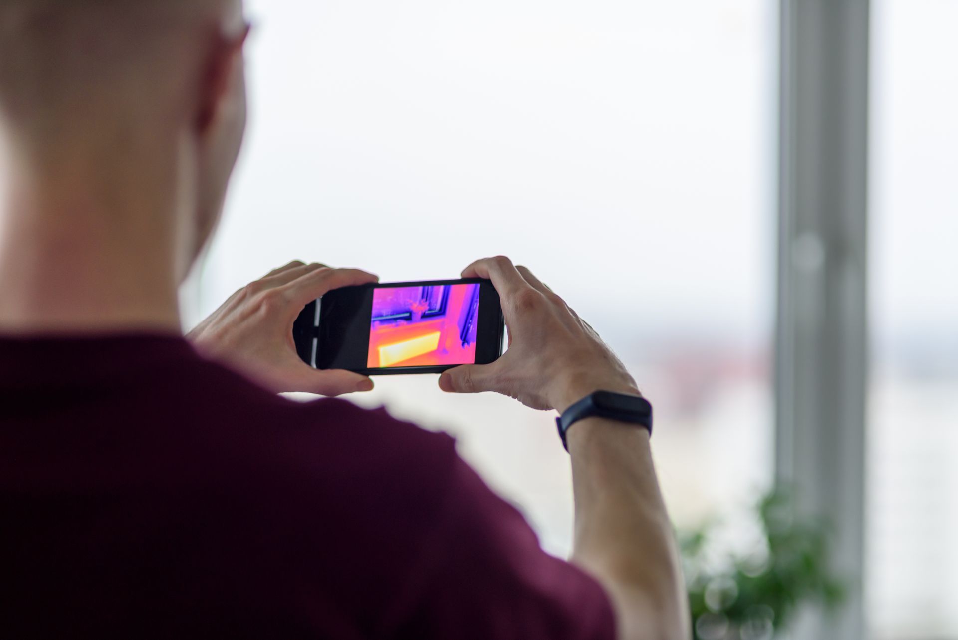 Person photographing a bright thermal image on a smartphone by a window