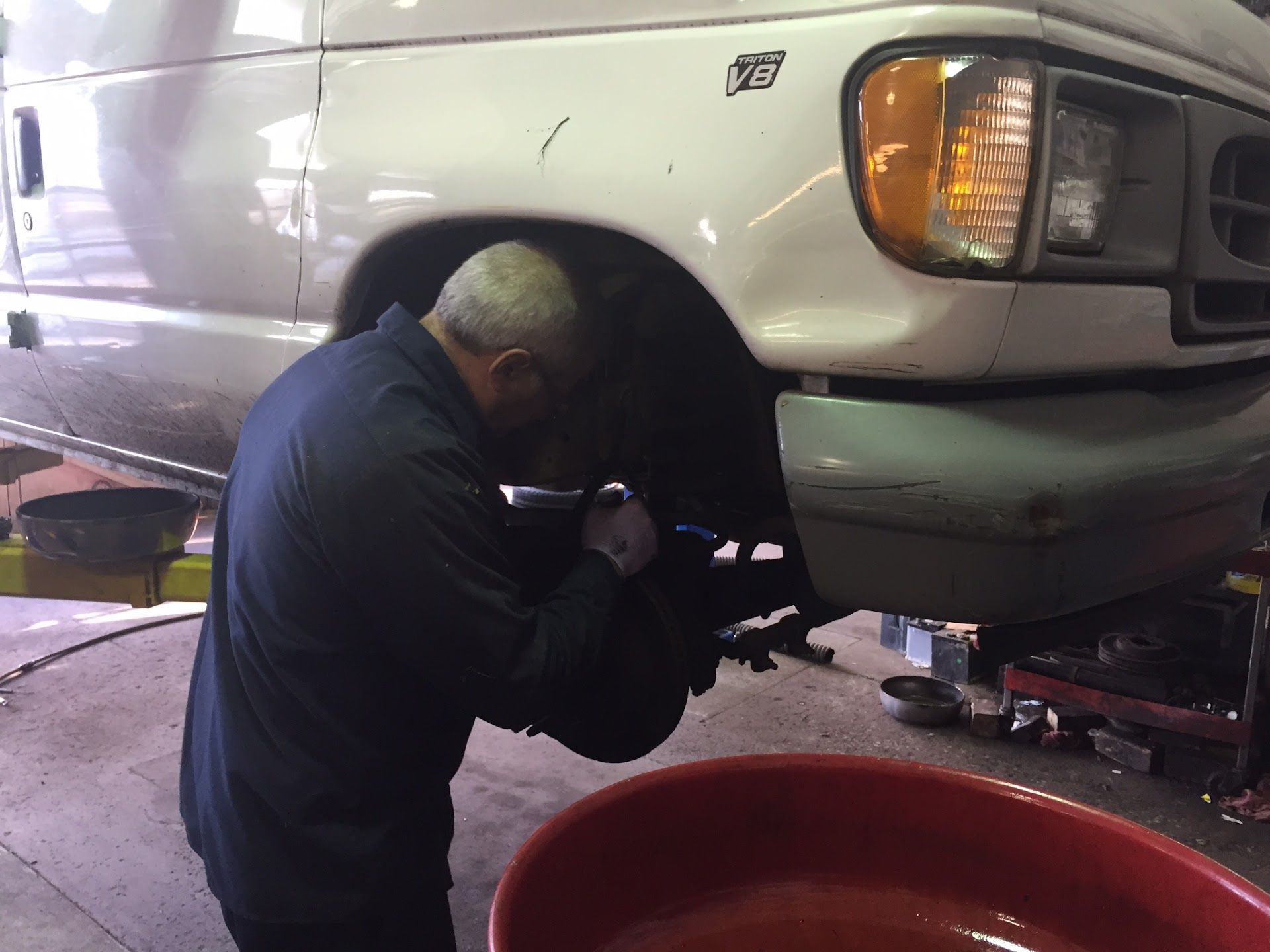 Mechanic working on the front wheel of a white van in a garage, using a tool. A red tub is on the floor.  | Aberdeen Automotive