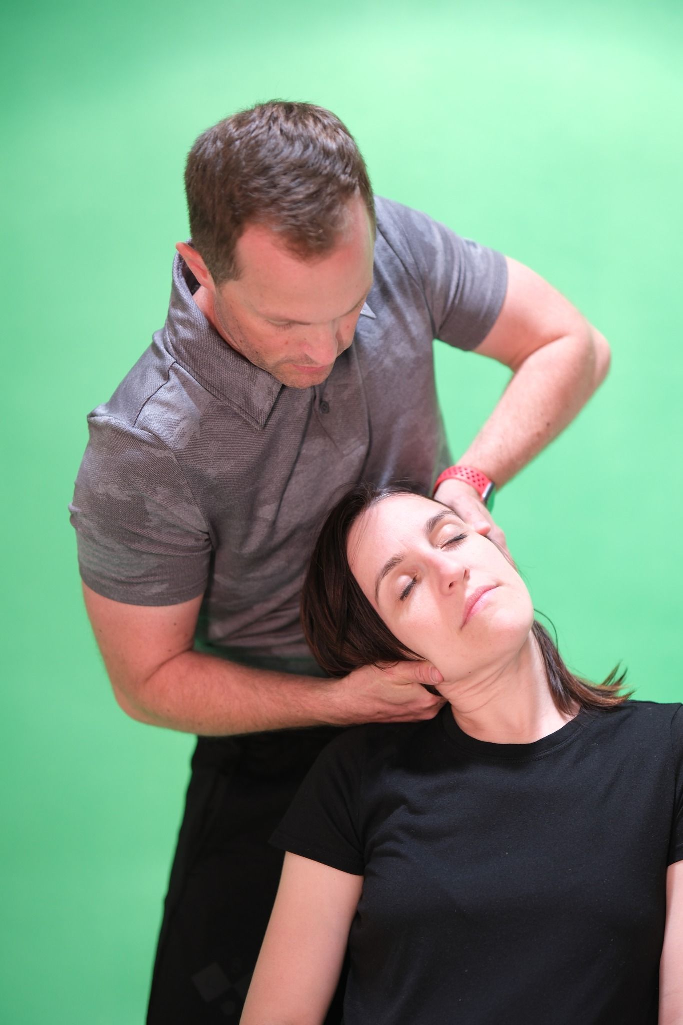 Chiropractor adjusting a woman’s neck against a green backdrop
