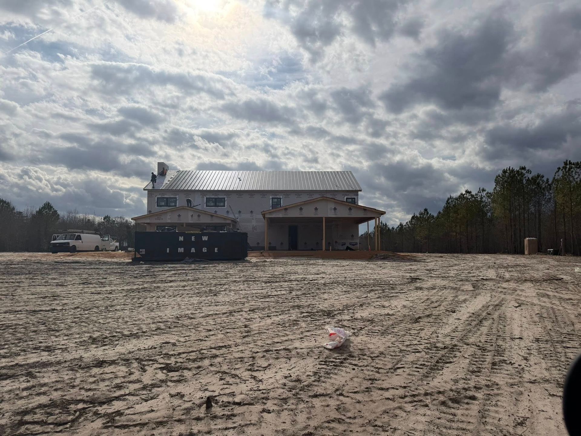 Sandy lot with a white building, black dumpster, and cloudy sky overhead