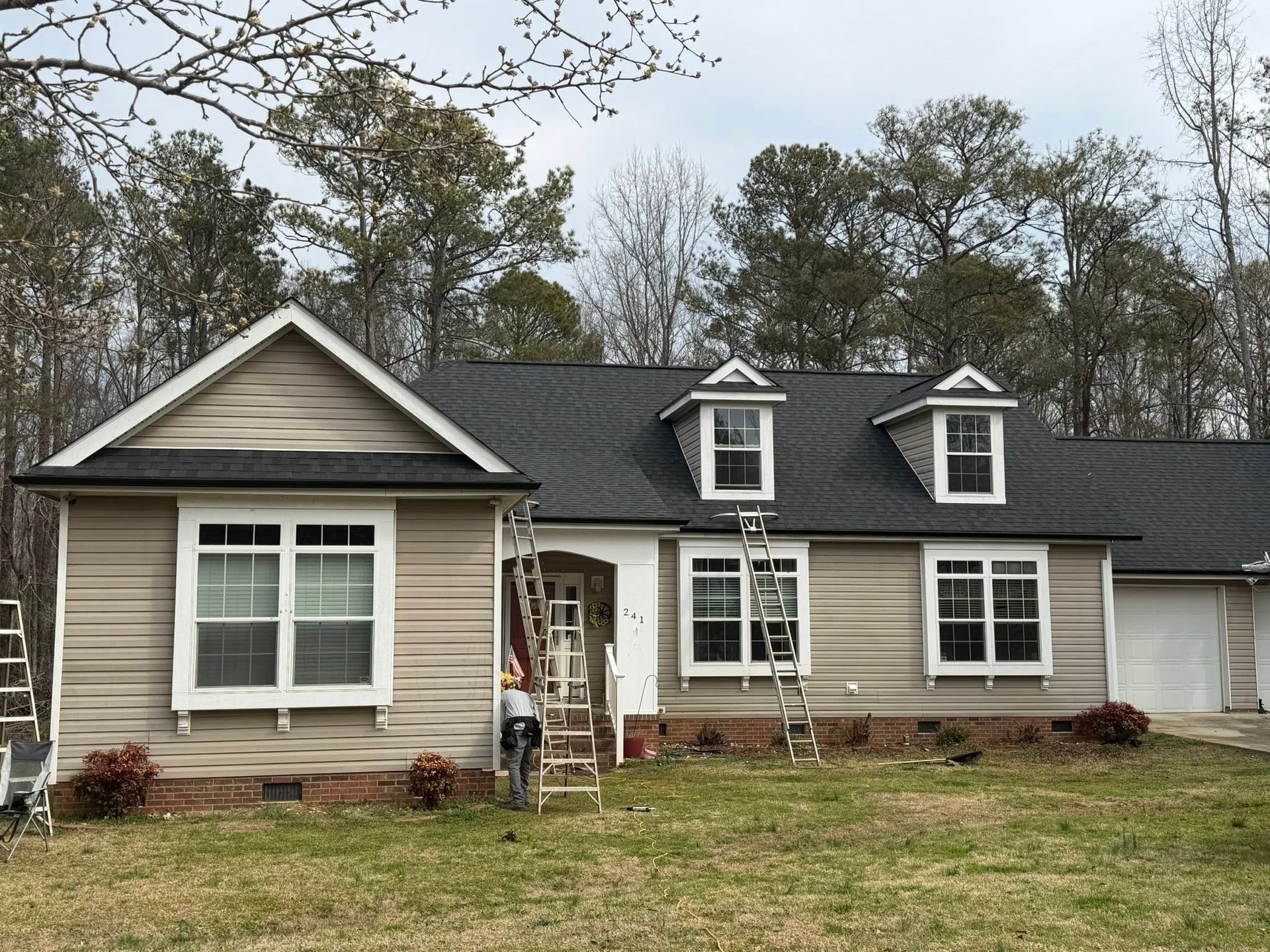 Suburban house with gray siding, black roof, and front yard under overcast sky