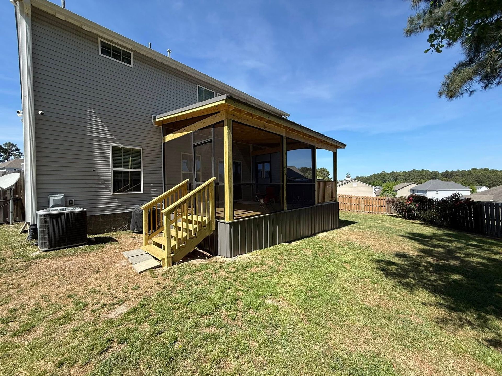 Backyard deck attached to a gray house, with yellow stairs and a covered porch under a blue sky.