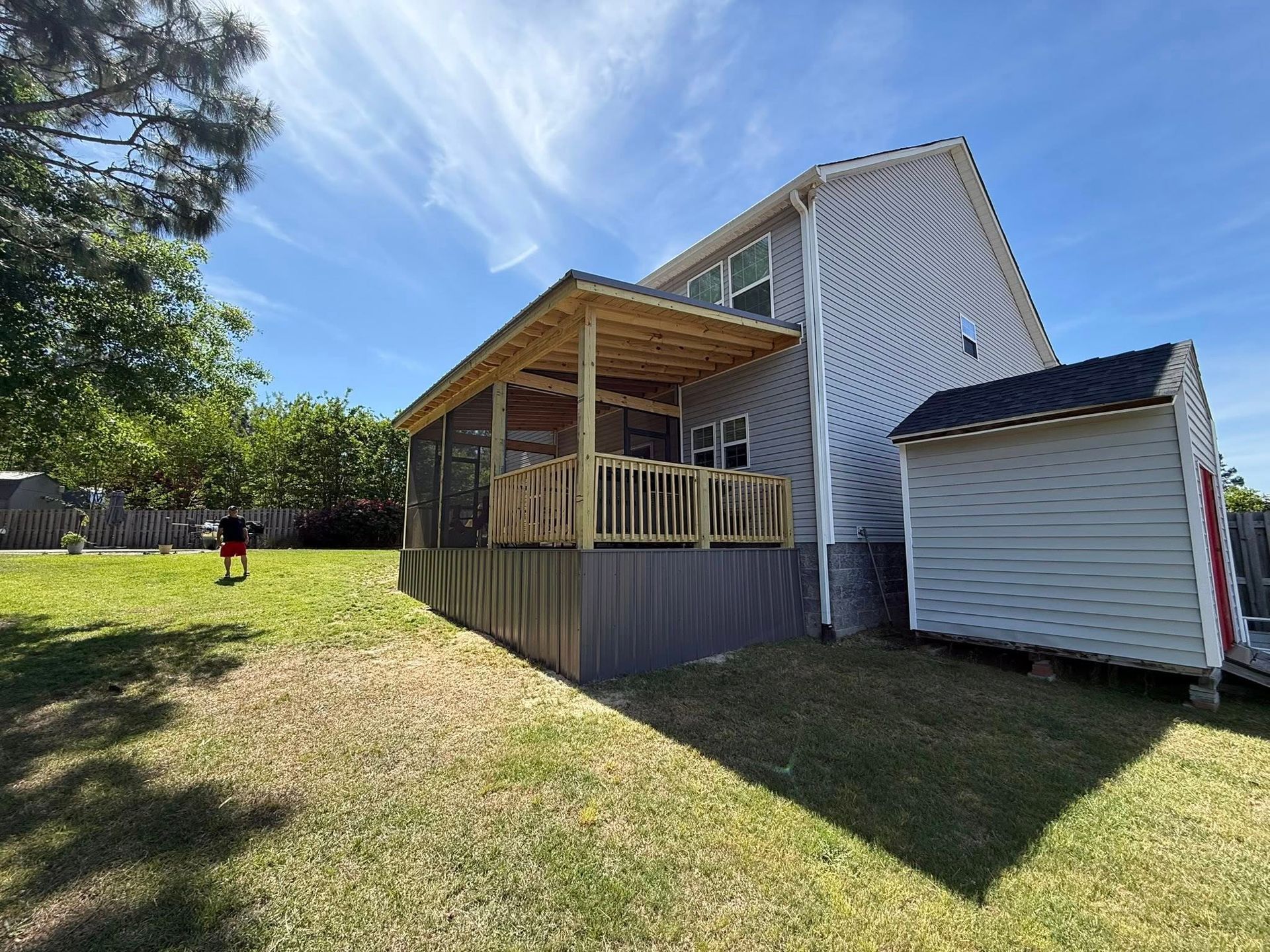 Backyard with a covered deck attached to a white house and a small shed in the sunlight