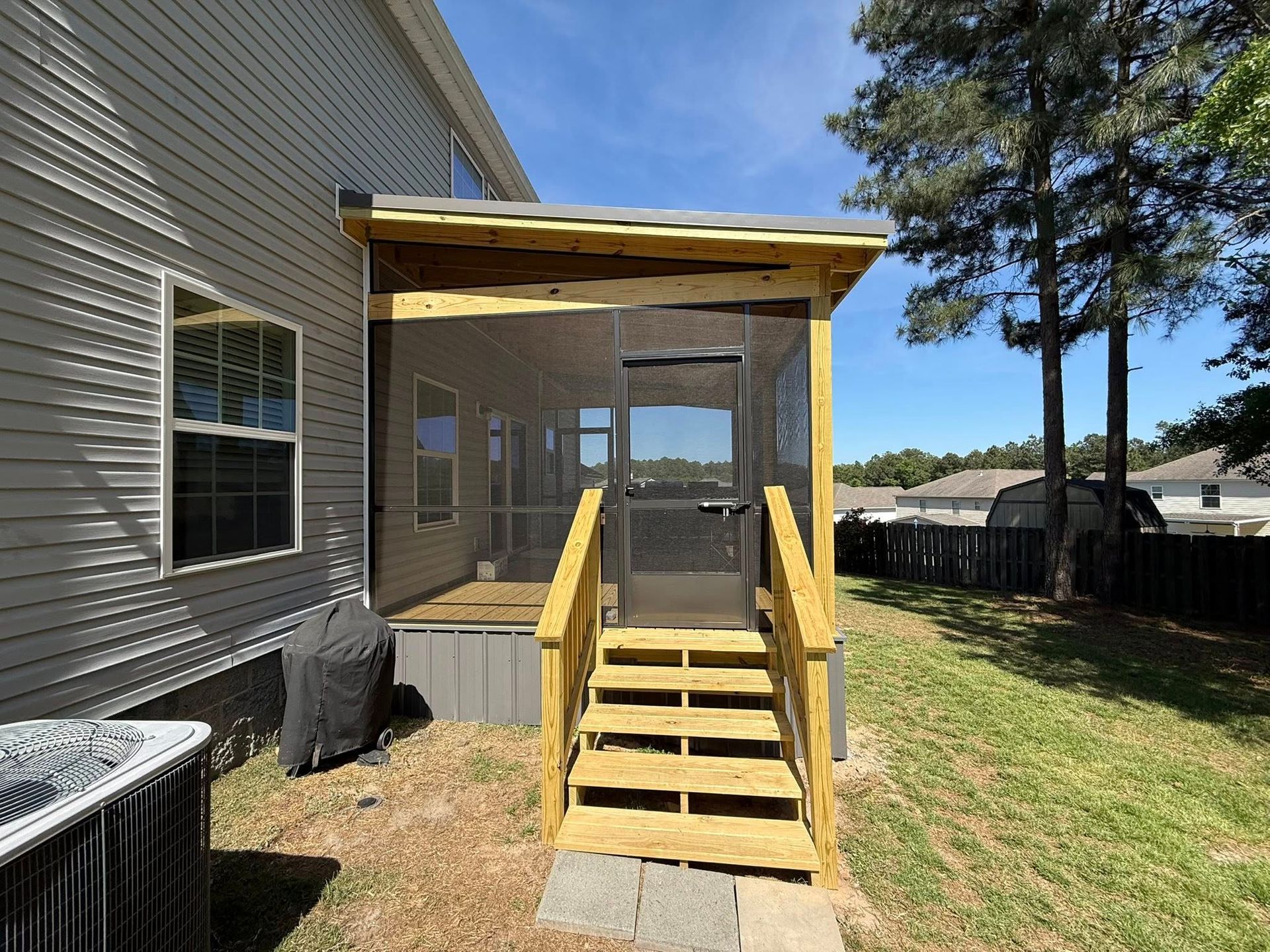Wooden porch and stairs added to the back of a gray house on a sunny day