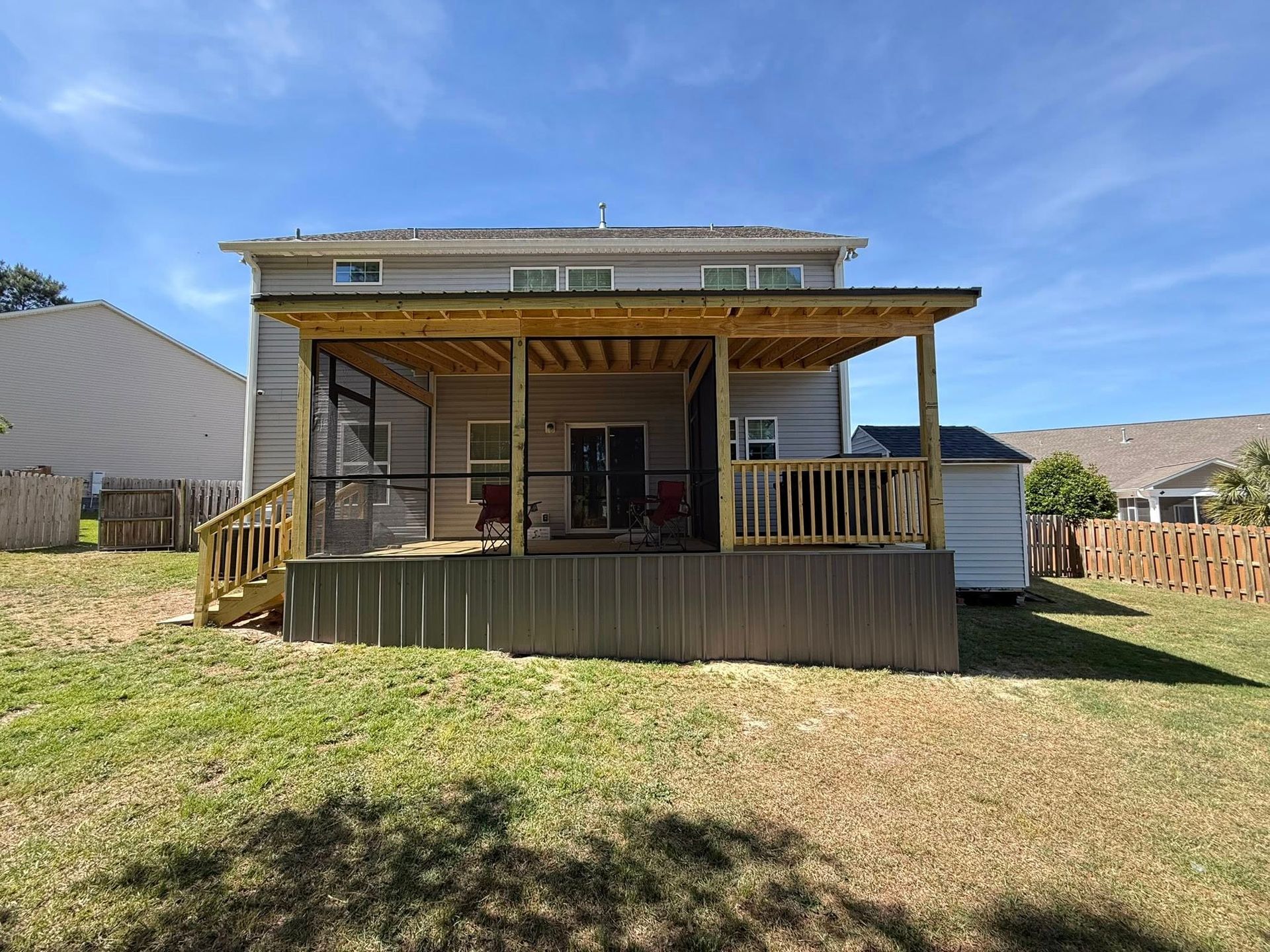 Backyard deck with wooden railing and roofed patio attached to a house, viewed from the lawn.