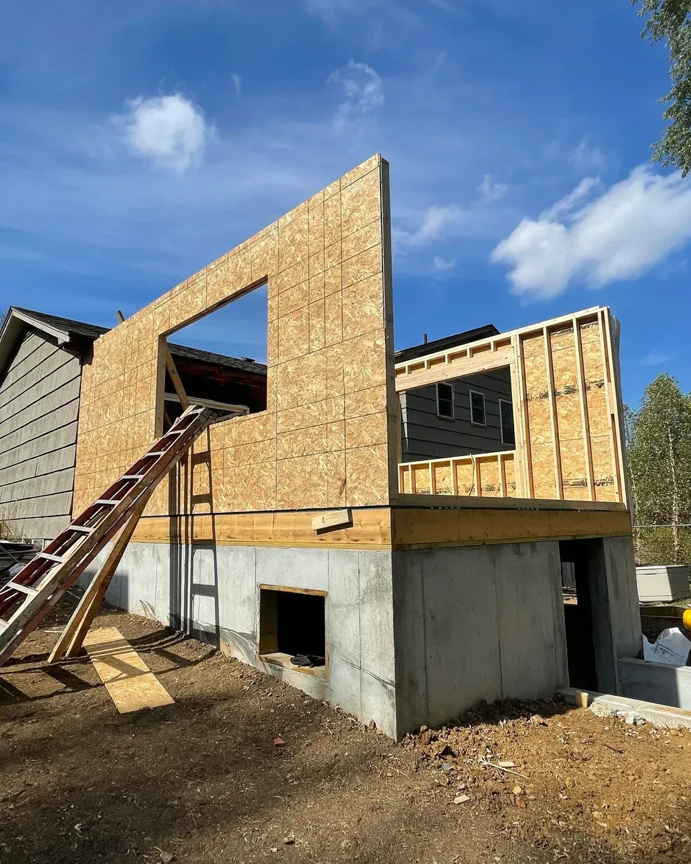 Partially framed house under construction with exposed wood, concrete foundation, and a ladder on the front.