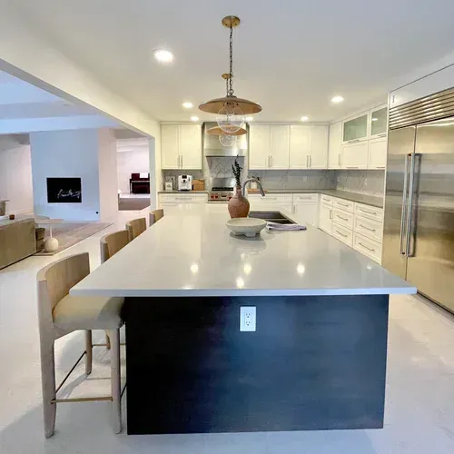 Bright modern kitchen with large white island, pendant light, and stainless steel refrigerator