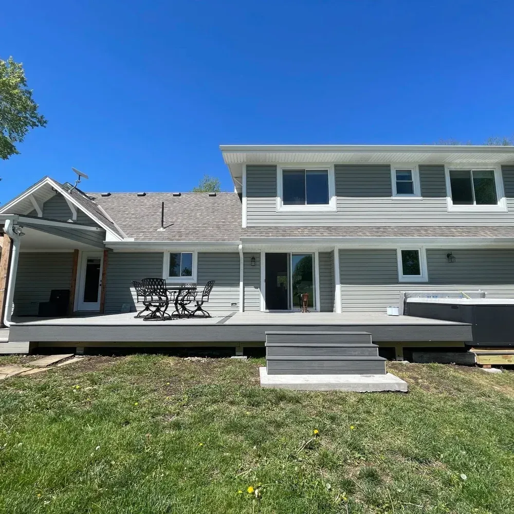 Suburban two-story house with a deck, patio table, and lawn under a clear blue sky