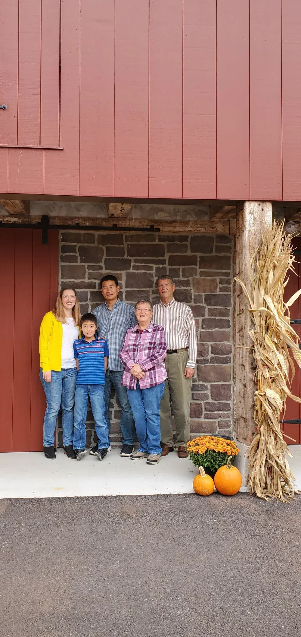 Family standing in a barn doorway beside hay bales and pumpkins