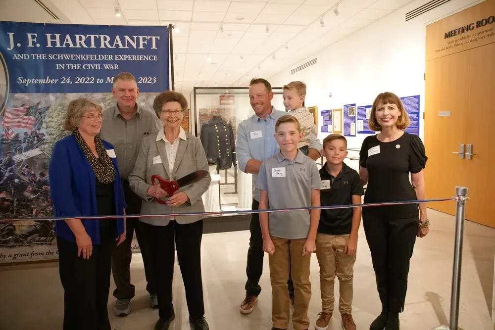 Seven people stand behind a ribbon in a hallway during a ribbon-cutting ceremony.