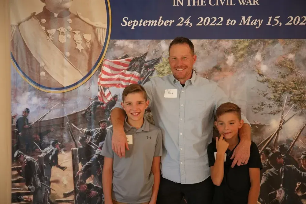 Three people posing in front of a Civil War exhibit banner and historical mural backdrop