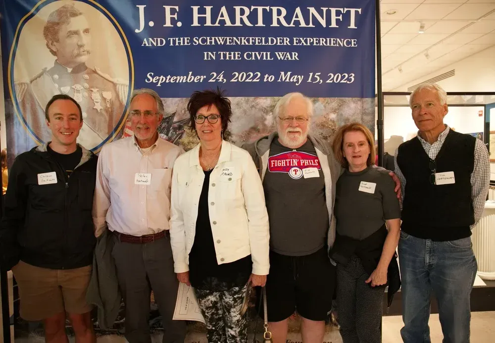 Five people posing in front of a J. F. Hartnett exhibit banner at a museum