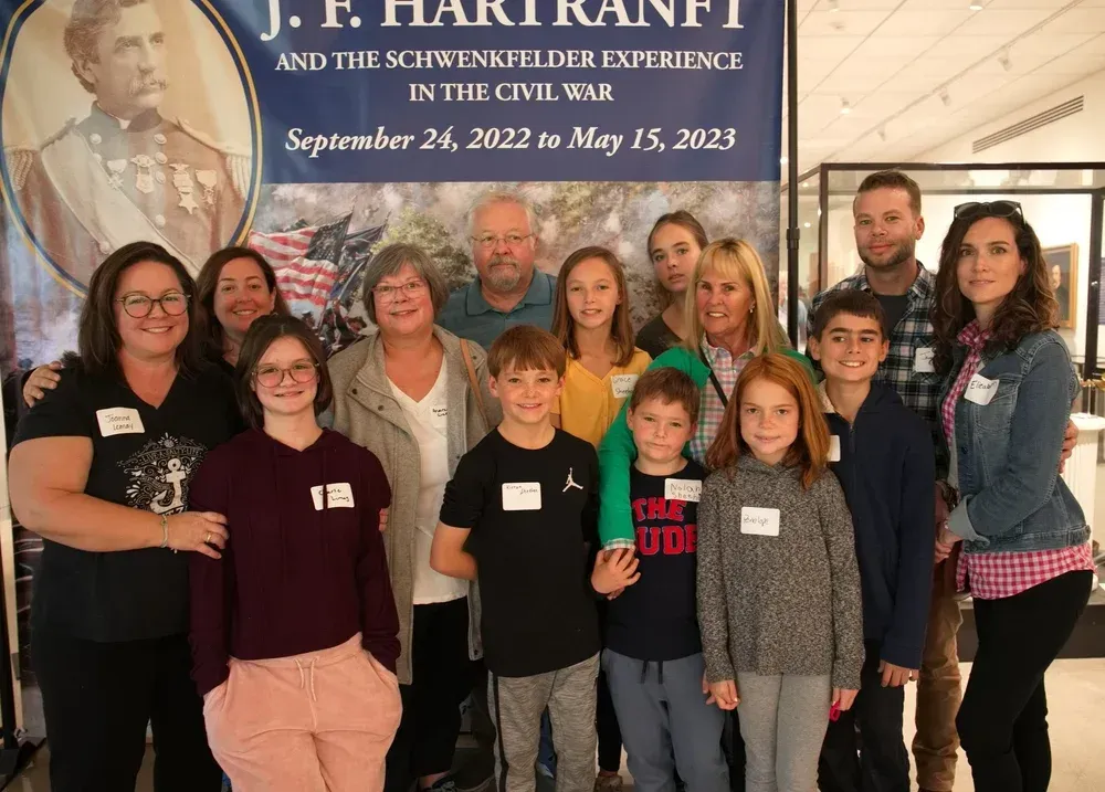 Group of people posing indoors in front of a J.F. Harriott banner, smiling at an event.