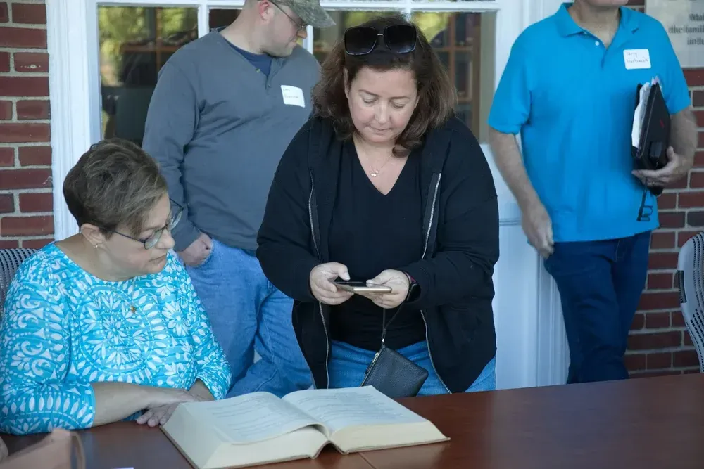 People reviewing a large open book at a table indoors, with one person holding a phone.