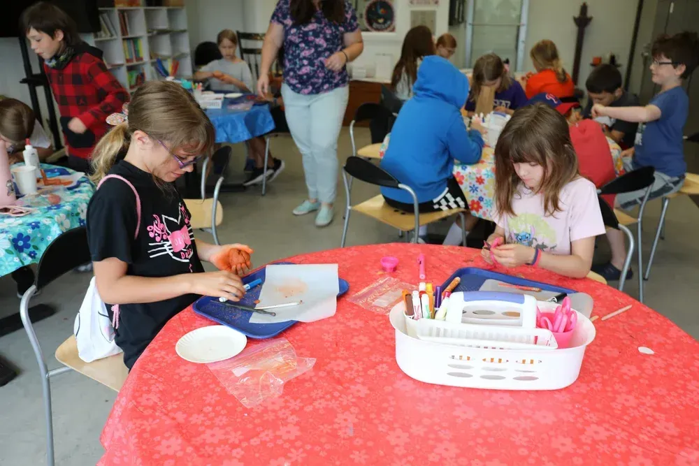 Children doing a craft activity at tables in a bright classroom with red tablecloths