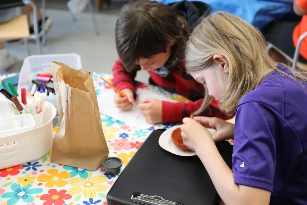 Children doing arts and crafts at a table with colorful supplies and paper shapes