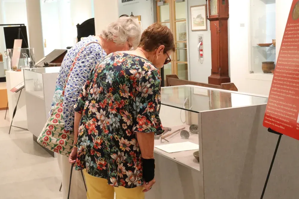 Two people lean over a museum exhibit display, reading information in a bright gallery.