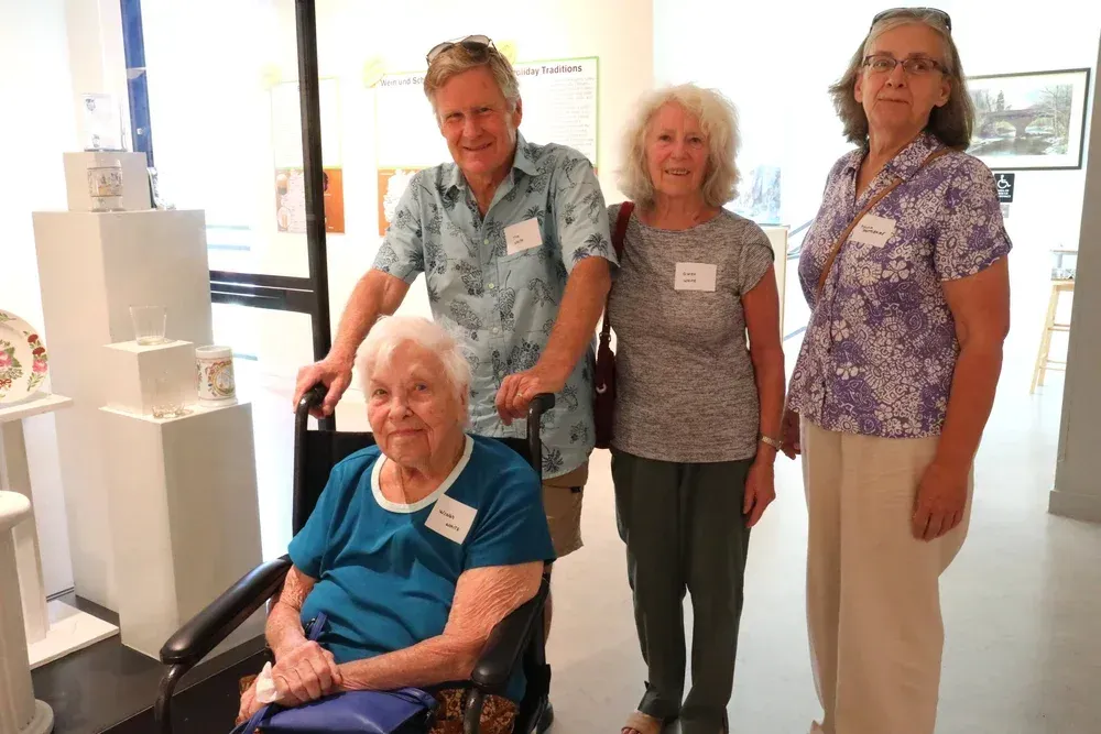 Four people standing indoors beside a seated man in a wheelchair near a white display model.