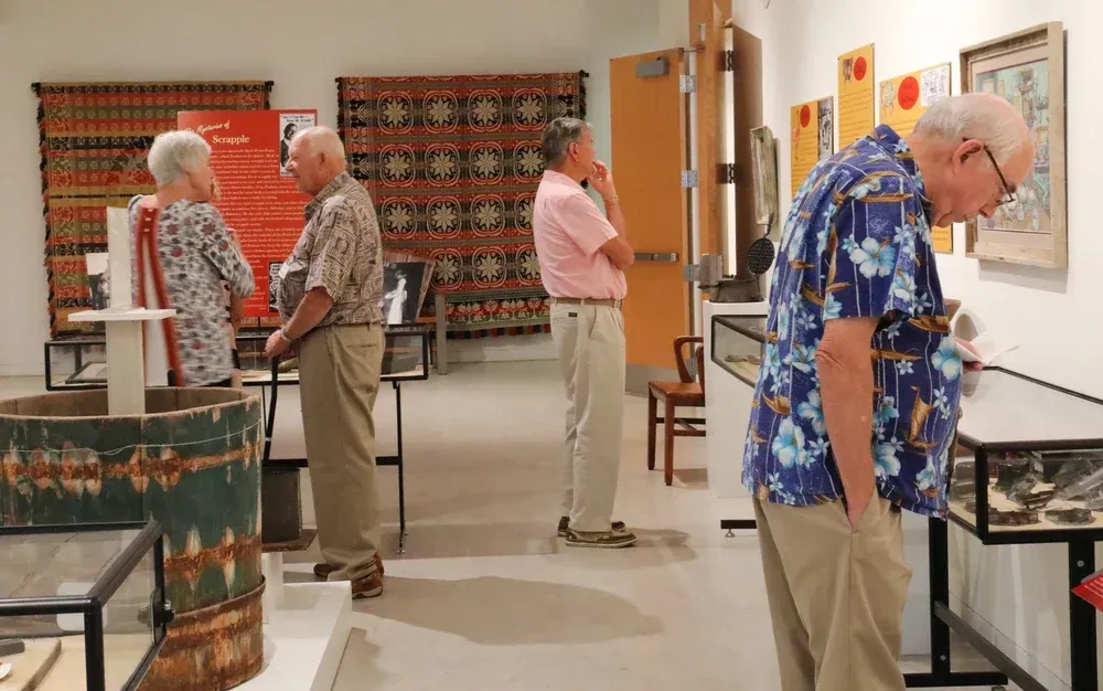 People browsing artwork in a gallery, with one man leaning over a display and others standing nearby.