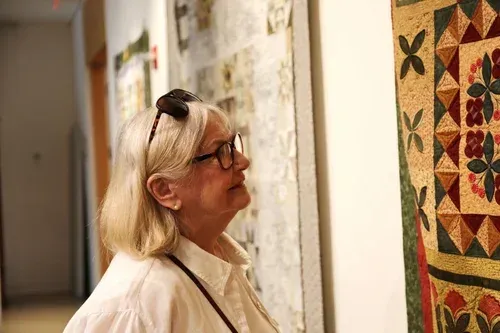 Woman viewing a colorful quilt display in a gallery hallway