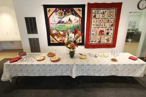 Decorated buffet table with cakes and flowers beneath two colorful wall hangings in a room