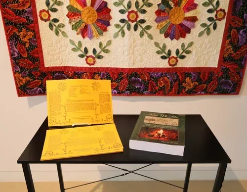Open book and another book on a black table beneath a colorful wall tapestry