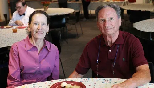 Two people seated at a table in a dining area, smiling at the camera.