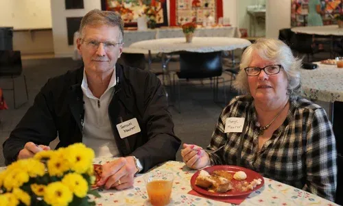 Two people seated at a table with flowers and snacks in a bright indoor gathering space