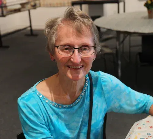 Smiling person in a turquoise top seated indoors at a table
