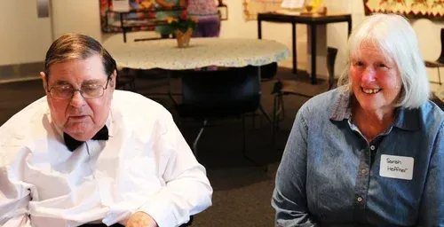 Two people seated indoors, smiling at a table in a warmly lit room
