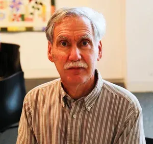 Man in a striped shirt looking at the camera in a softly lit indoor room
