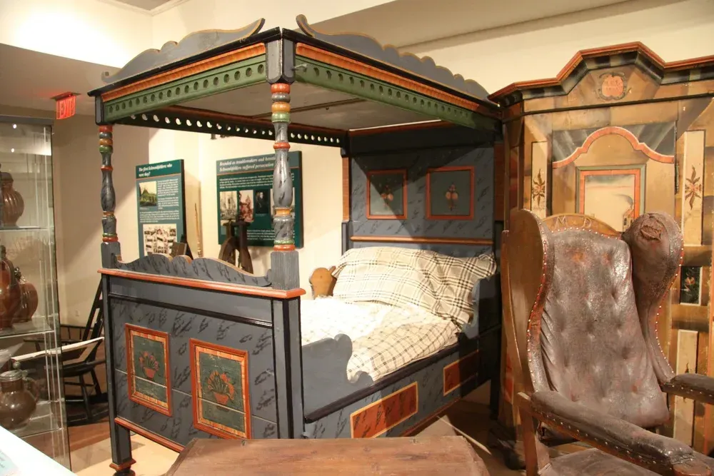 Ornate four-poster bed with colorful painted panels in a museum room