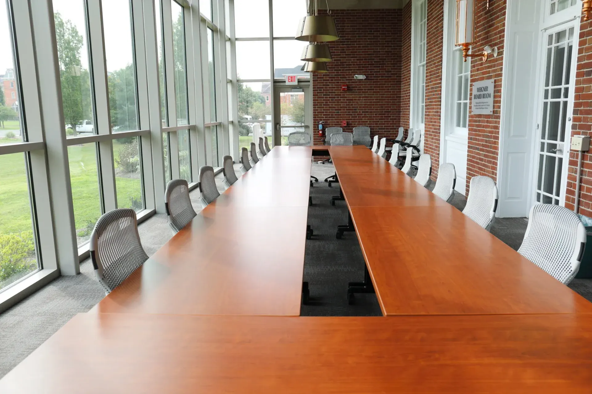 Long wooden conference table in a bright glass-walled meeting room