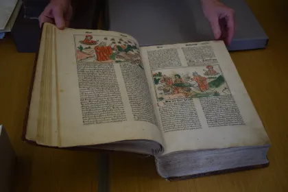 An open illustrated book on a table, with hands resting nearby.