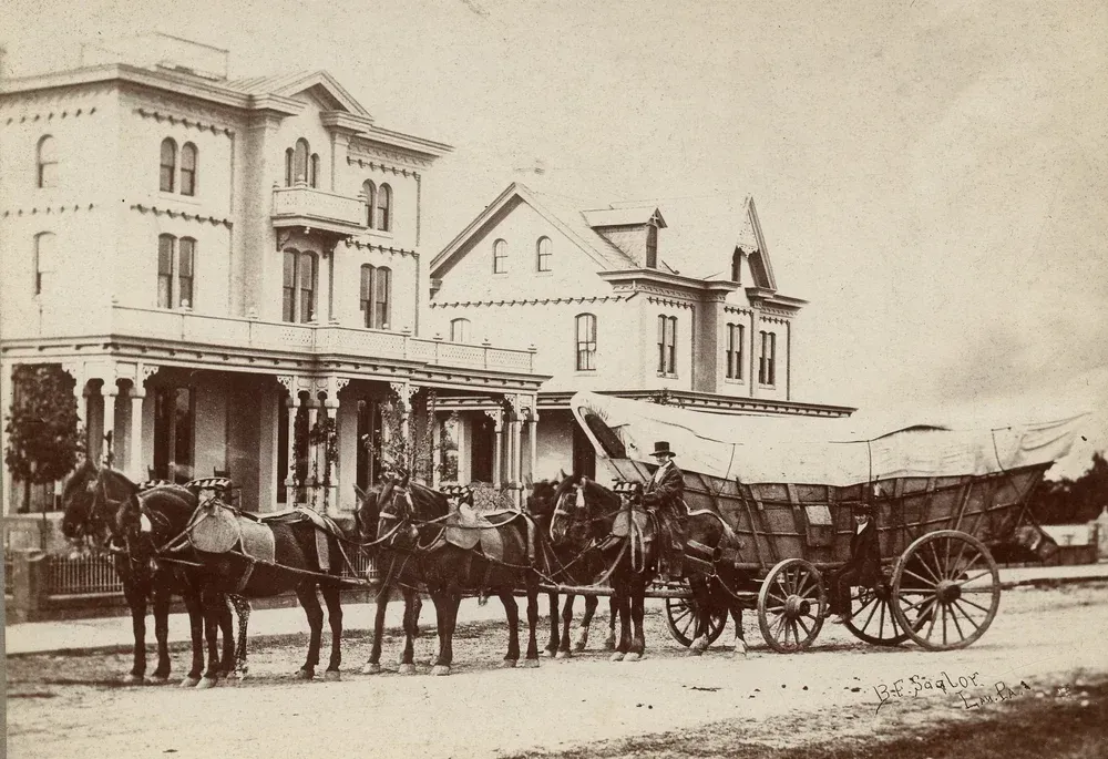 Sepia street scene with horse-drawn wagons parked outside a corner building