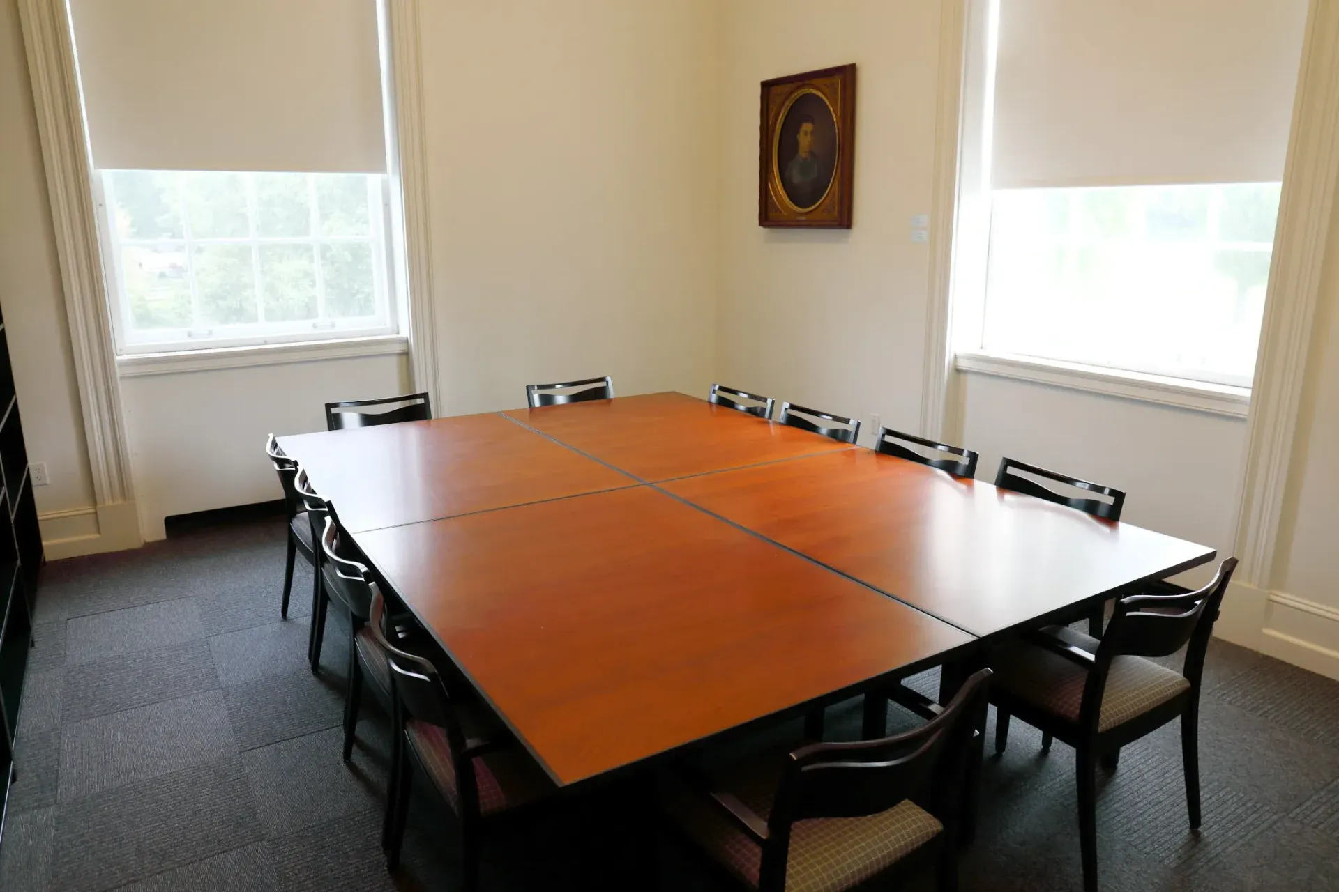 Conference room with a large wooden table, black chairs, and windows on two walls.