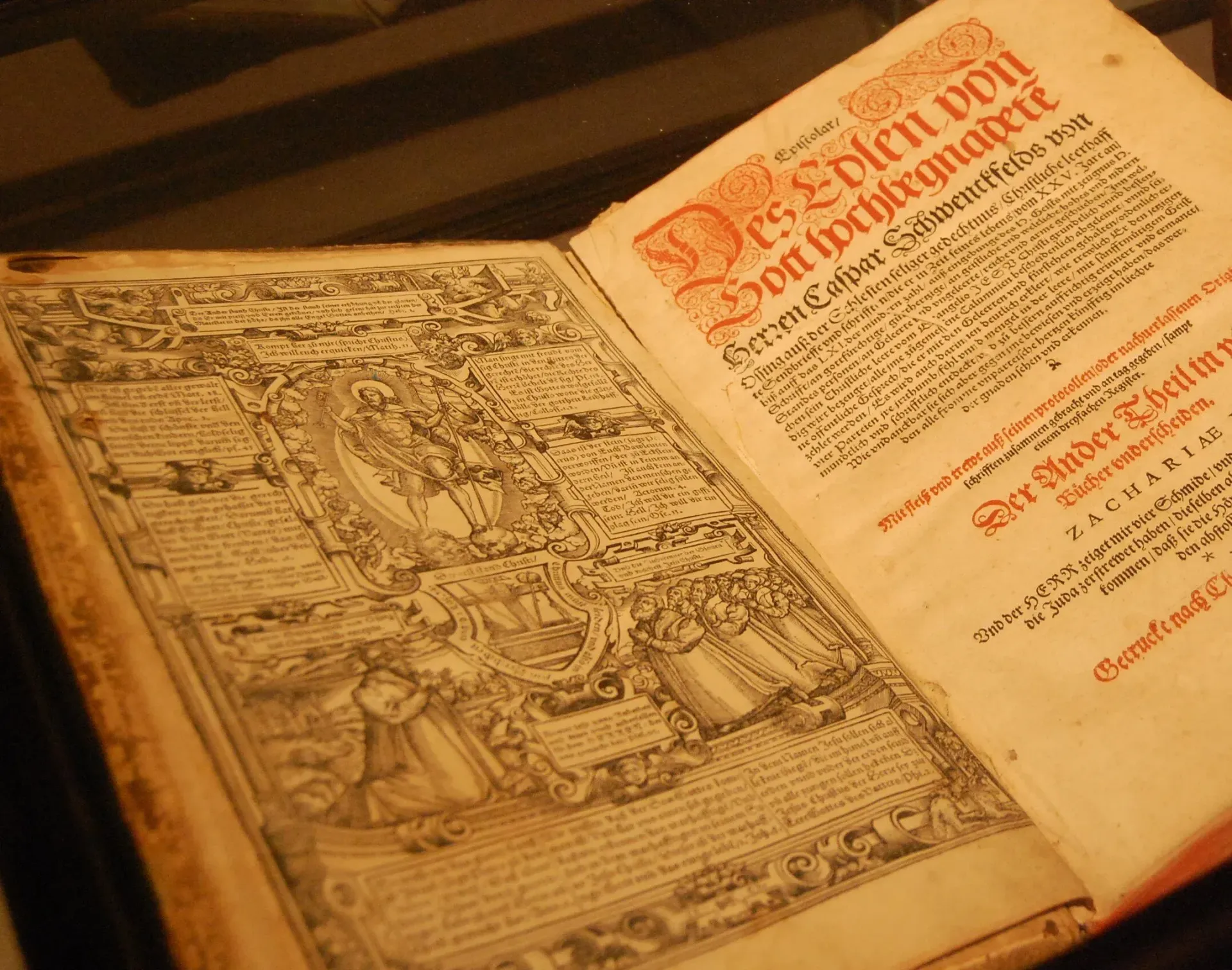 Open old book with ornate black-and-white illustration and red decorative text on yellowed pages
