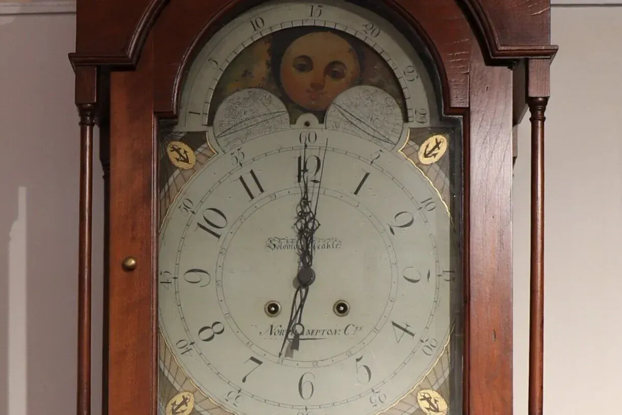 Antique wooden wall clock with a white face and Roman numerals, showing around 12:01.