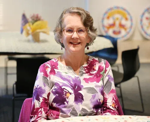 Smiling woman in a purple and pink floral top seated at a table in a casual indoor setting