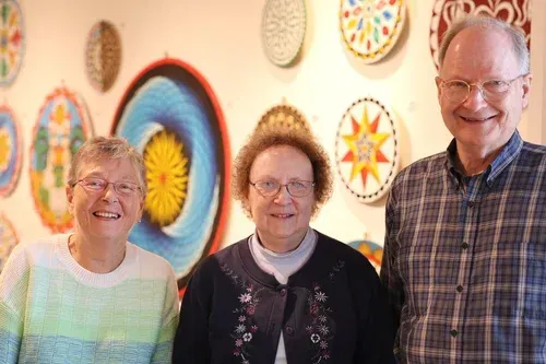 Three smiling people standing in front of colorful circular wall art.