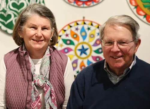 Two people smiling indoors before a colorful circular pattern backdrop