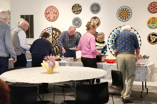 People gathered around craft tables in a bright room with colorful wall art.