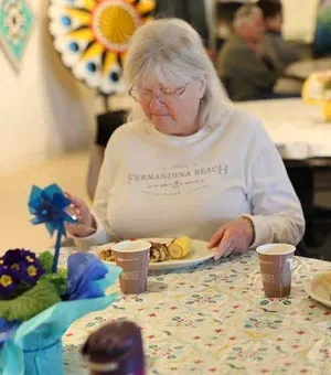 Woman seated at a table with a plate and two cups in a decorated indoor gathering