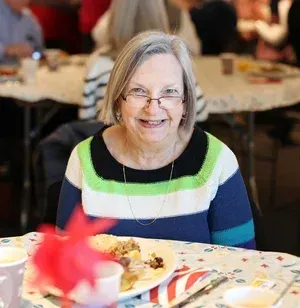 Smiling woman in a striped sweater seated at a table with a plate of food at a social gathering