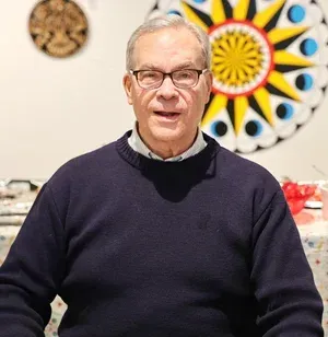Man in glasses and dark sweater seated indoors with colorful circular wall art behind him